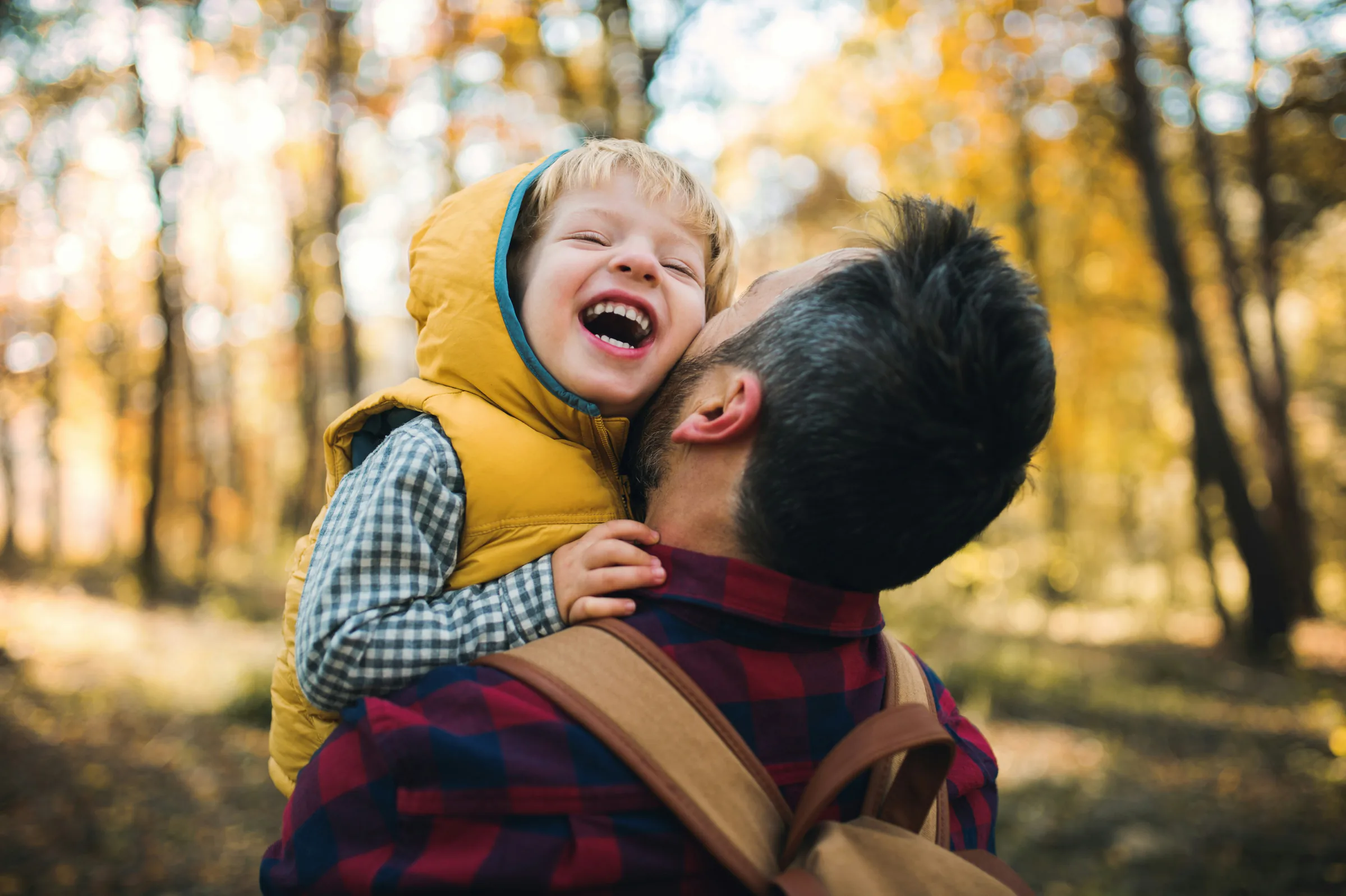 Child laughing on a parent's shoulders in autumn woodland